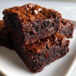 Close-up of two stacked, incredibly fudgy brownies with melted chocolate chips on top.