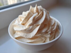 A close-up of fluffy, piped vanilla buttercream frosting swirled high in a small white bowl.