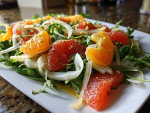 Close-up of a vibrant citrus salad featuring segments of red grapefruit, orange, arugula, and shaved fennel on a white plate.
