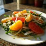 Close-up of a vibrant citrus salad featuring orange and grapefruit segments over arugula and thinly sliced onions.