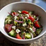 Close-up of a vibrant lentil salad featuring green lentils, cherry tomatoes, cucumber, red onion, and feta cheese.