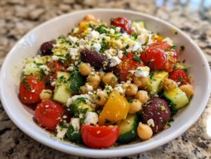 A close-up of a vibrant Mediterranean chickpea salad featuring chickpeas, cherry tomatoes, cucumber, olives, and feta cheese.