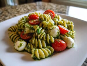 Close-up of a serving of pesto pasta salad featuring fusilli pasta, cherry tomatoes, and small mozzarella balls.