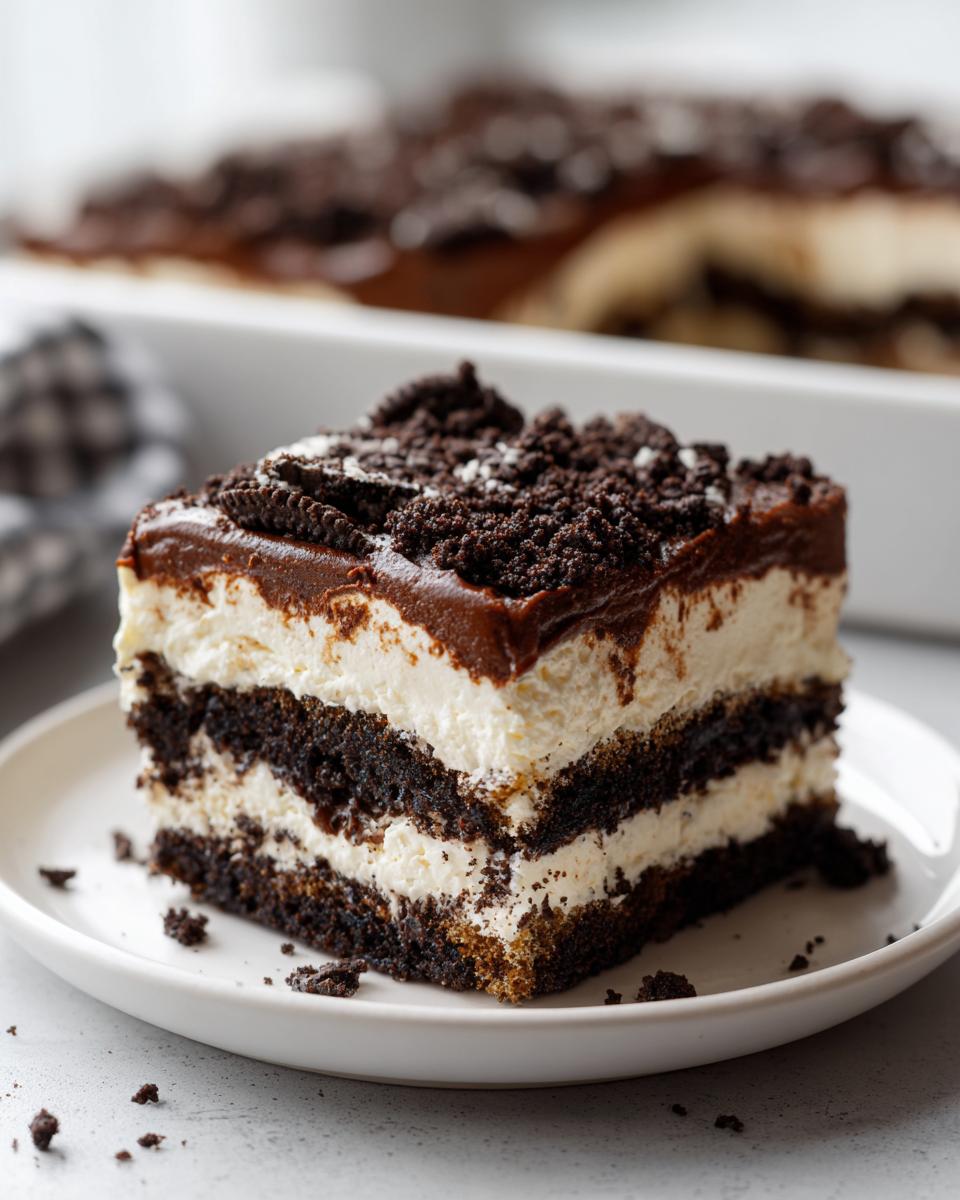 A layered square slice of rich dirt cake featuring dark chocolate layers, white cream filling, and crushed cookie topping.