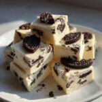 A stack of creamy white squares of Oreo fudge loaded with dark chocolate cookie pieces and topped with mini Oreo halves.