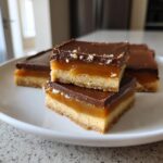 Close-up of stacked, homemade Twix bars showing the shortbread, caramel, and chocolate layers.