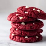 A close-up stack of four vibrant red velvet cake mix cookies dotted with white chocolate chips.