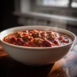 Close-up of a steaming white bowl filled with rich, hearty chili containing ground meat and kidney beans.