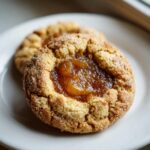 Close-up of a freshly baked apple pie cookies, featuring a cinnamon-sugar crust and a dollop of apple filling in the center.