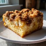 Close-up of a square slice of baked french toast with a thick, cinnamon streusel topping on a white plate.