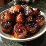 A white bowl filled with rich, dark brown candied yams glistening in a thick, sweet syrup.