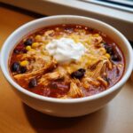 Close-up of a bowl of rich chicken taco soup topped with melted cheese, corn, black beans, and sour cream.
