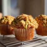 Close-up of a moist pistachio muffin topped with a generous, golden crumb topping and visible pistachio pieces.