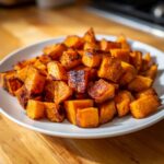 A close-up of perfectly caramelized, cubed roasted sweet potatoes piled high on a white plate.