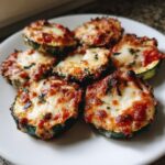 Close-up of six baked zucchini pizza bites topped with melted, slightly browned mozzarella and tomato sauce.