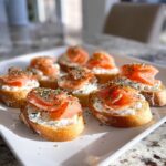Close-up of several smoked salmon bites served on toasted bread with cream cheese and herbs.
