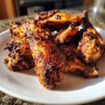 Close-up of baked Jamaican jerk chicken wings with a rich, dark, spicy crust on a white plate.