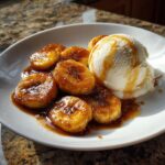 A serving of caramelized bananas foster next to a scoop of vanilla ice cream drizzled with sauce.