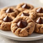 A close-up of several freshly baked kiss cookies rolled in sugar, each topped with a melted chocolate kiss.