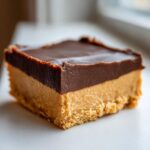 A single, rich square of buckeye fudge showing a crumbly base, thick peanut butter layer, and smooth chocolate topping.