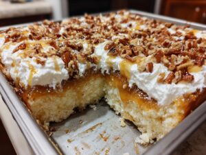 A square of butter pecan praline poke cake showing the moist cake base, caramel filling, whipped topping, and chopped pecans.
