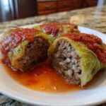 Close-up of two halved cabbage rolls showing the ground meat and rice filling, topped with tomato sauce.