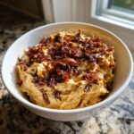 A creamy, light brown caramelized onion dip topped generously with dark, rich caramelized onions in a white bowl.