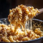 A spoonful of hot, cheesy french onion pasta showing extreme cheese pull and topped with caramelized onions.