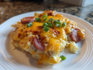 A close-up of a slice of pierogi casserole topped with melted cheddar cheese, sliced sausage, and green onions.
