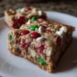 Close-up of a chewy Christmas cookie bars slice topped with red, green, and white candies and chips.
