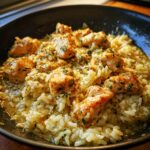 Close-up of pan-seared chicken pieces served over creamy garlic parmesan rice, garnished with parsley.