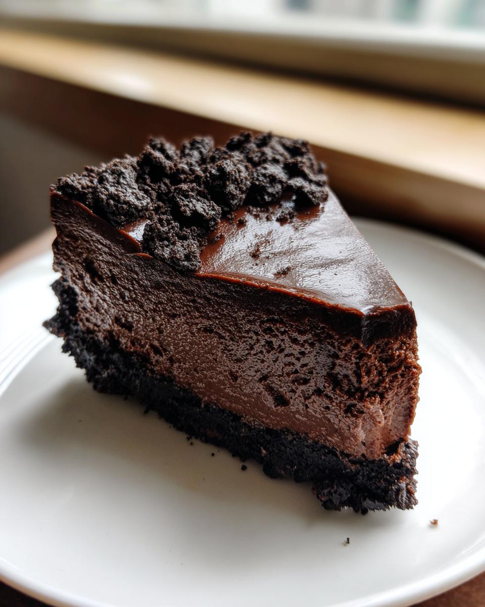 A decadent, dark slice of chocolate cheesecake with a crumb topping on a white plate.