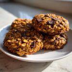 A stack of four golden brown, chunky chocolate chip breakfast cookie treats resting on a white plate.