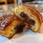 Close-up of a chocolate croissant cut in half, showing flaky layers and gooey, melted chocolate filling.