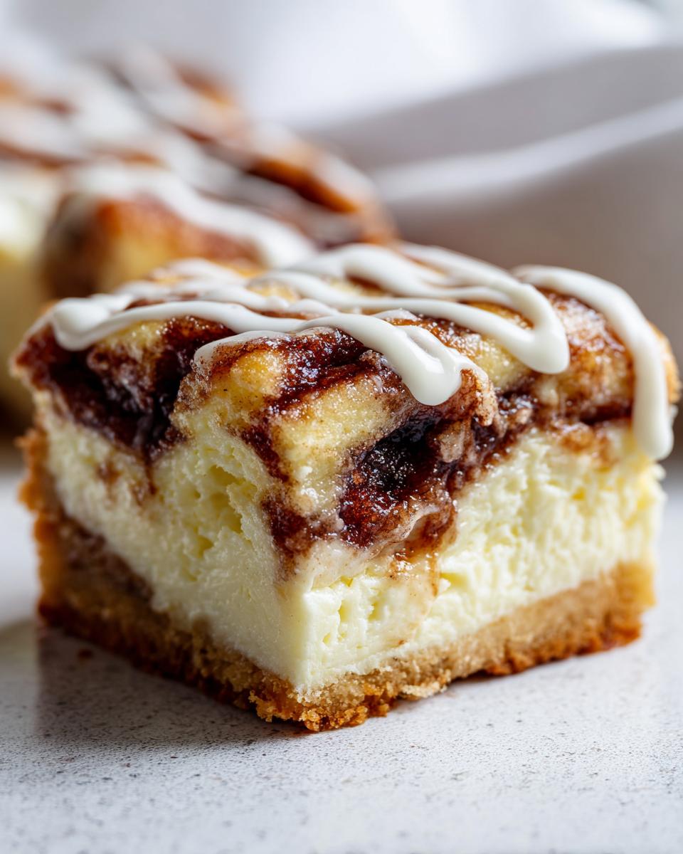 Close-up of a rich slice of cinnamon roll cheesecake showing the creamy filling, cinnamon swirl, and white icing drizzle.