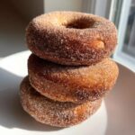 A stack of three delicious baked pumpkin donuts coated generously in cinnamon sugar.
