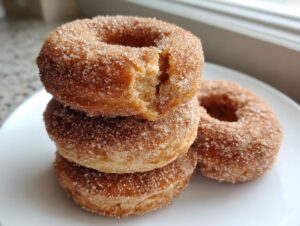 A close-up stack of three cinnamon sugar coated baked pumpkin donuts on a white plate.