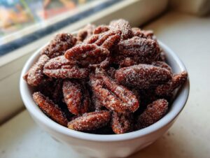 Close-up of a white bowl filled with glistening cinnamon sugar pecans, coated heavily in sparkling sugar crystals.
