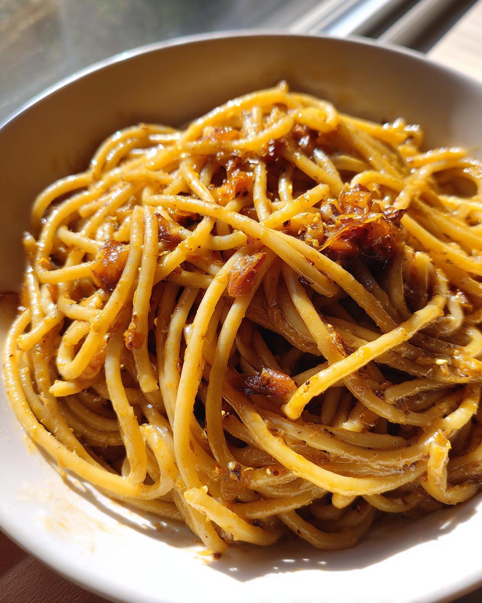 Close-up of glossy, saucy garlic noodles tossed with browned bits of garlic and seasoning, served in a white bowl.