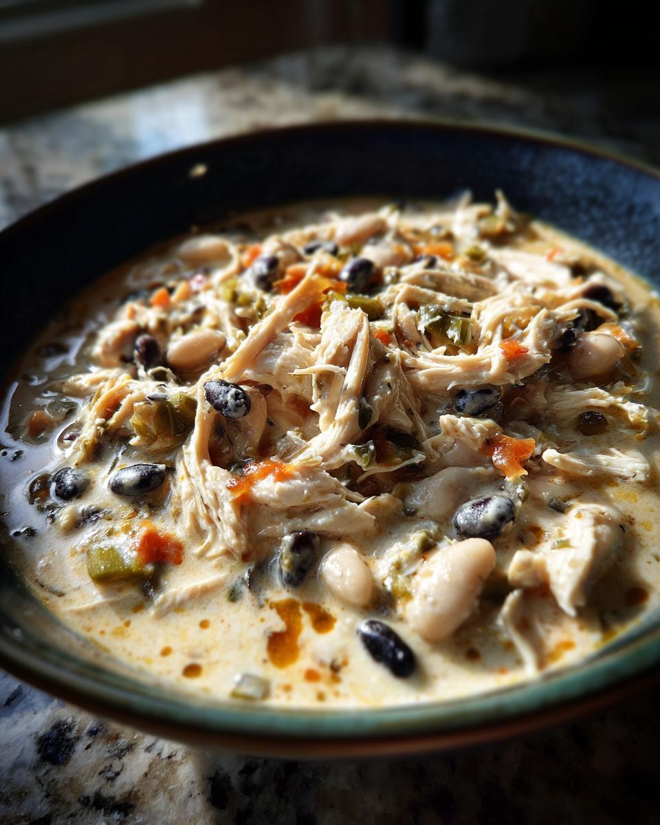 Close-up of a hearty bowl of cream cheese chicken chili featuring shredded chicken, black beans, and white beans.