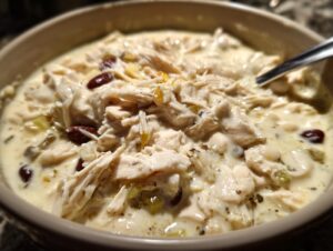A close-up, appetizing view of creamy white cream cheese chicken chili loaded with shredded chicken and dark red kidney beans.