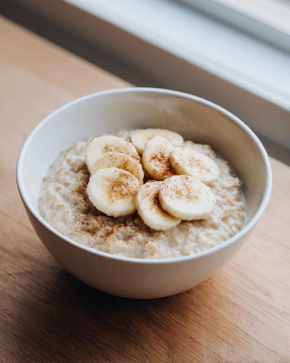 A white bowl filled with creamy banana oatmeal, topped with sliced bananas and a sprinkle of cinnamon.