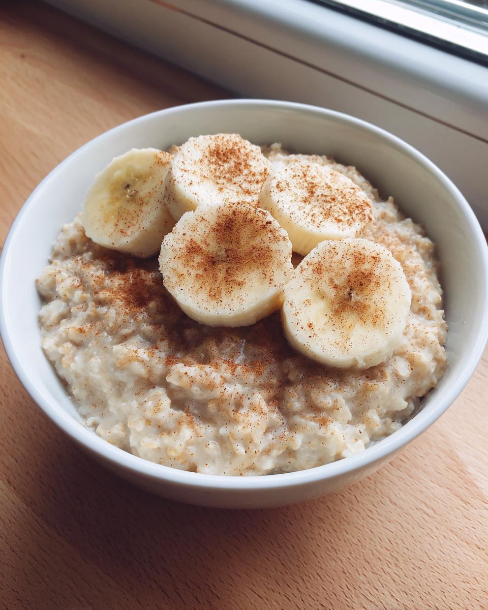 A white bowl filled with creamy banana oatmeal, topped with sliced bananas and a dusting of cinnamon.