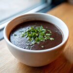 A close-up of a bowl of rich, dark black bean soup garnished with fresh chopped cilantro.