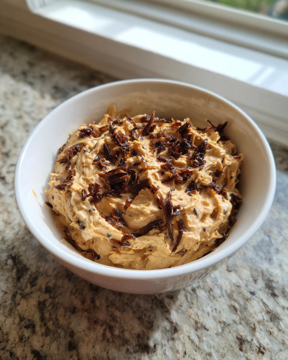 A white bowl filled with creamy caramelized onion dip, topped generously with crispy, dark caramelized onions.