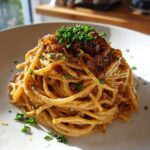 A close-up of creamy caramelized onion pasta, topped generously with dark caramelized onions and fresh parsley.