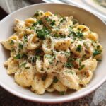 A close-up of a white bowl filled with creamy chicken pasta, topped with fresh parsley and grated cheese.