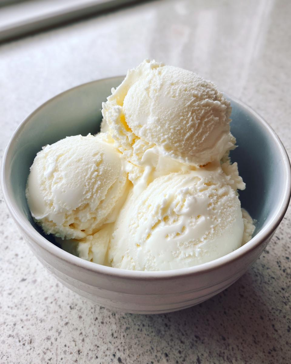 Three scoops of smooth, white cottage cheese ice cream served in a light blue bowl on a speckled countertop.