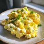 Close-up of creamy, bright yellow egg salad recipe garnished with chopped green onions and black pepper.