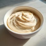 Close-up of a creamy, pale yellow fruit dip swirled beautifully in a small white bowl.